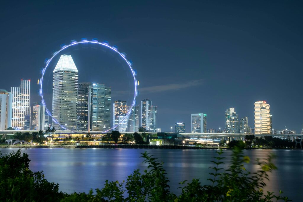 Beautiful night view of Singapore skyline with illuminated Ferris wheel and reflections on the river.