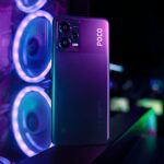 Poco smartphone displayed vertically with a neon lit gaming setup in the background.