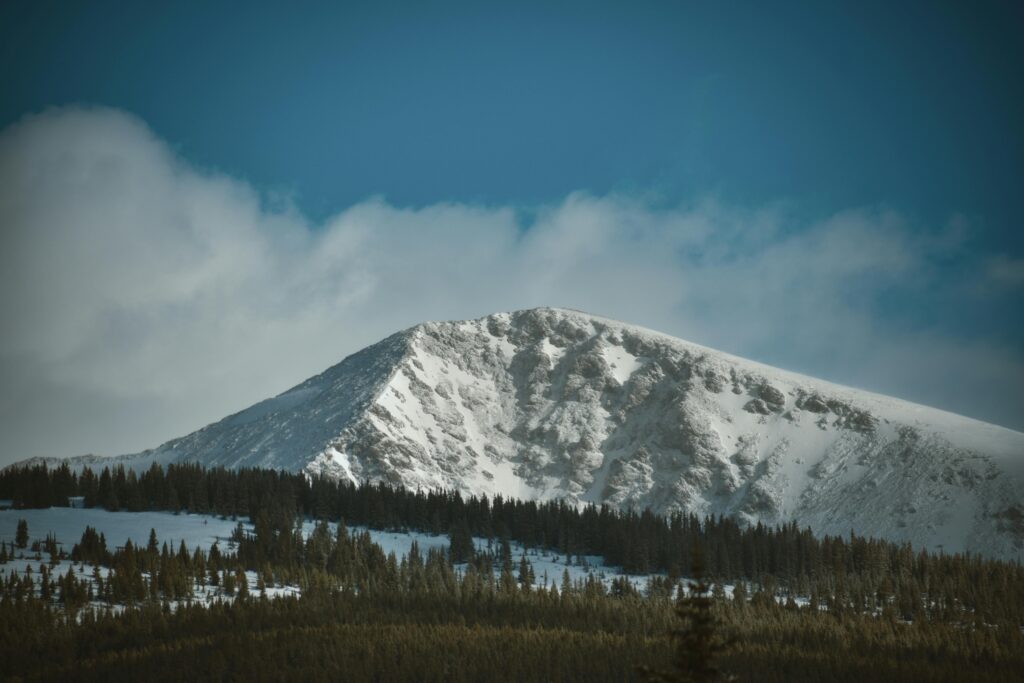 A stunning view of a snow-covered mountain peak surrounded by evergreen trees in the Rocky Mountains.