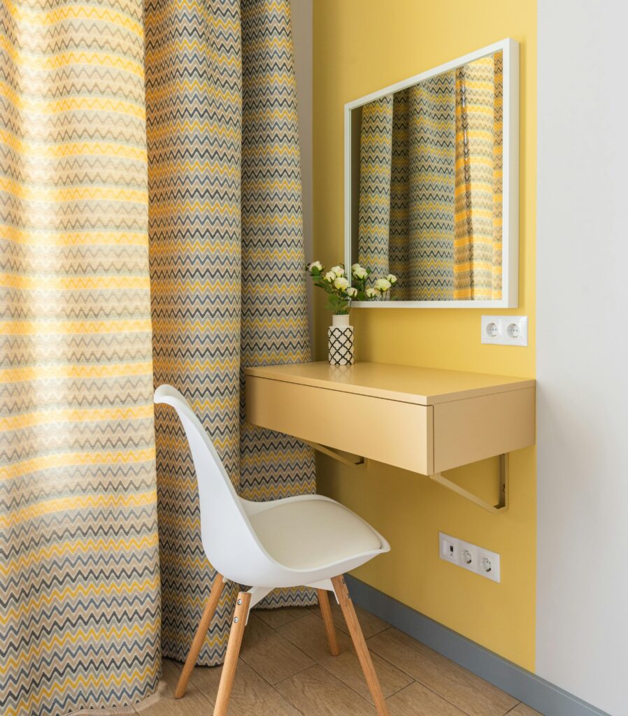 Elegant corner vanity setup with mirror, yellow zigzag curtains, and modern chair.