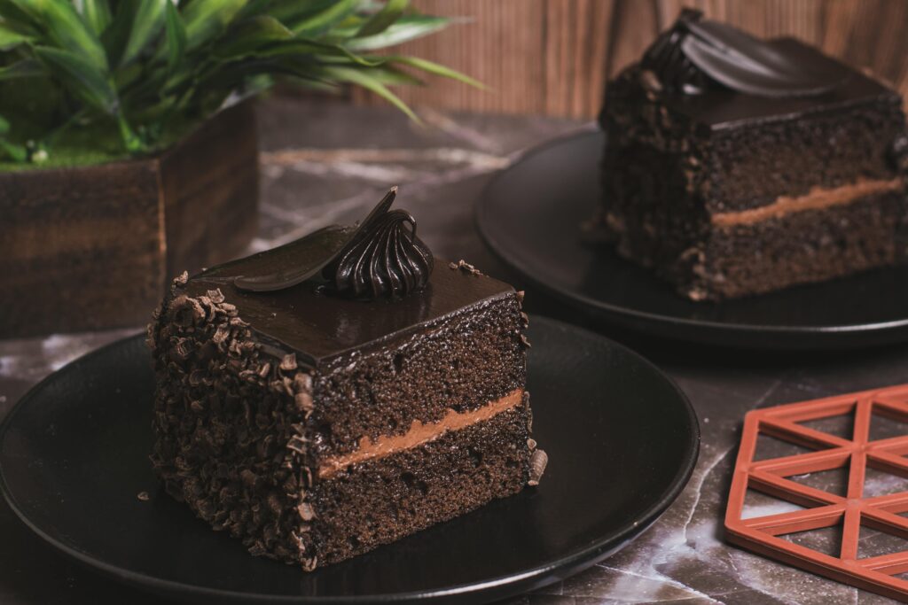 Rich chocolate cake slices with frosting adorned on black plates, perfect for desserts and food photography.