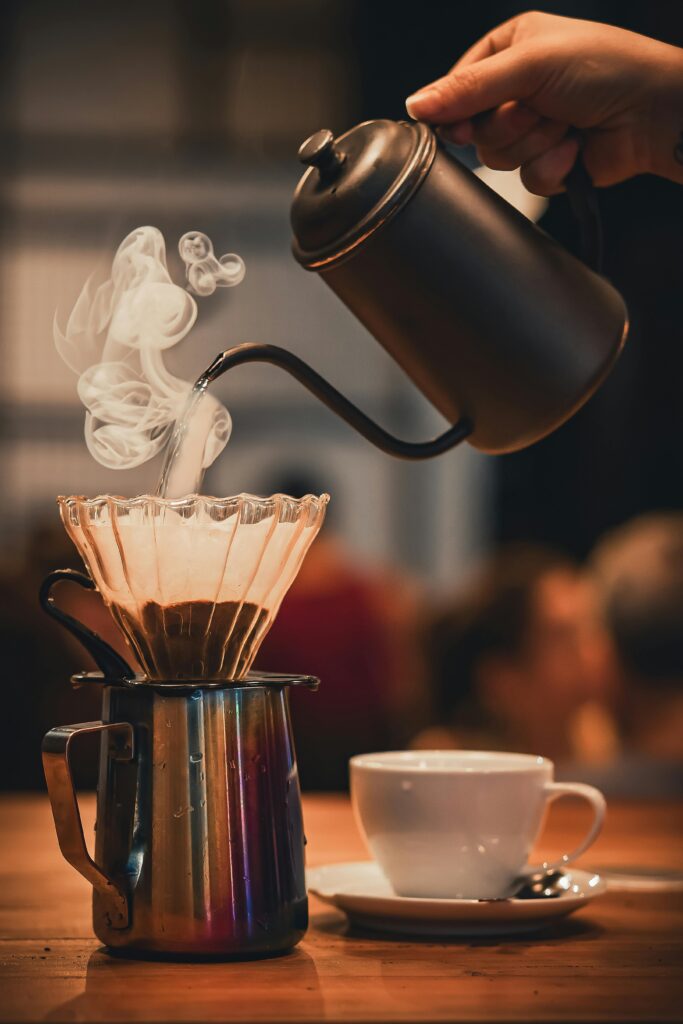 A barista pouring hot coffee with a steaming kettle over a filter in a cozy Rio de Janeiro cafe.