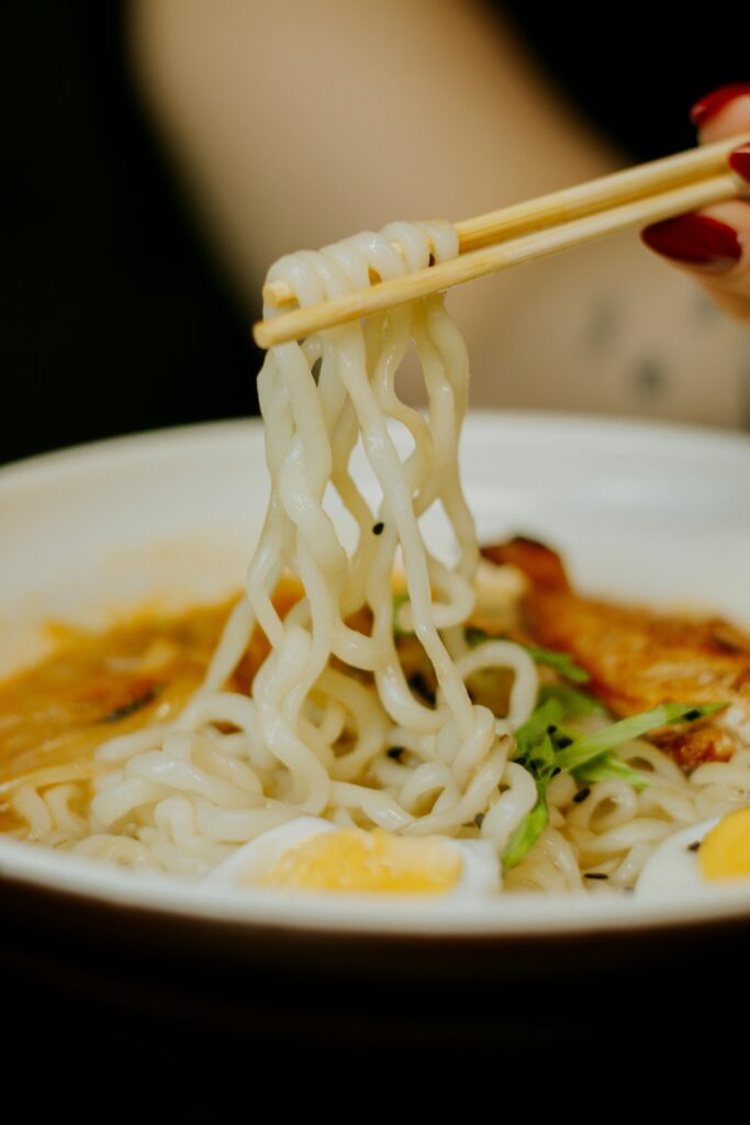 Delicious bowl of Asian noodles being lifted with chopsticks, perfect for dining themes.