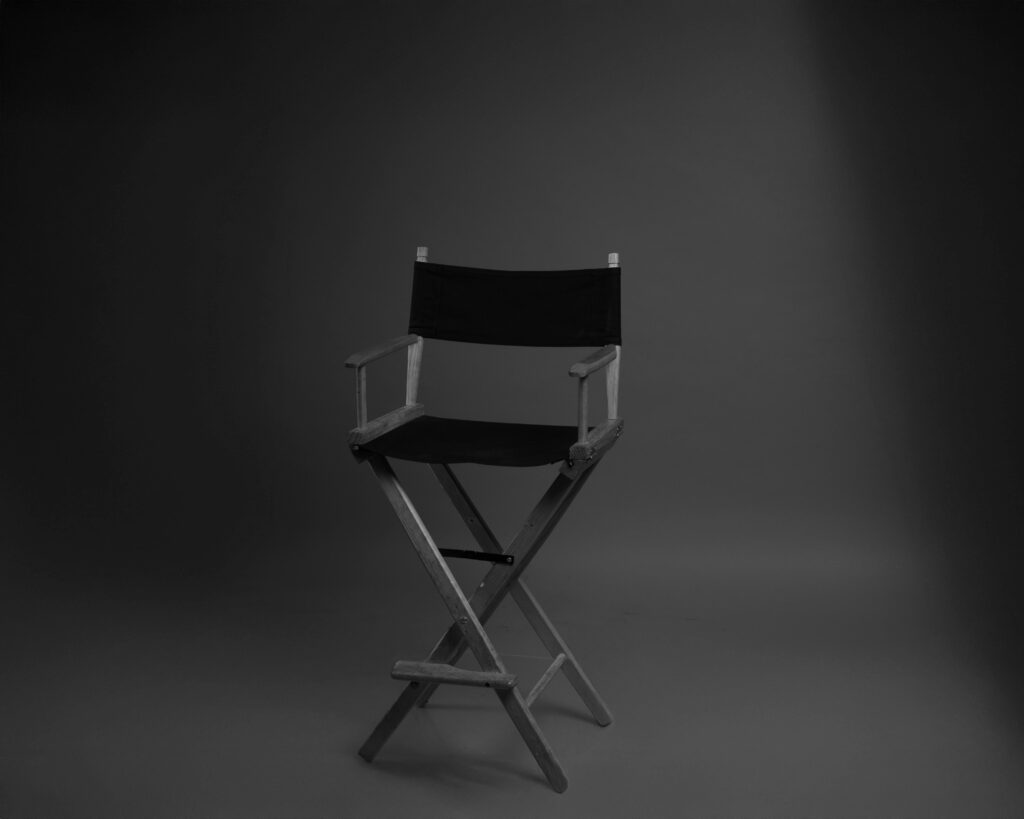 A black and white photo of a director's chair in a minimalist studio setting.