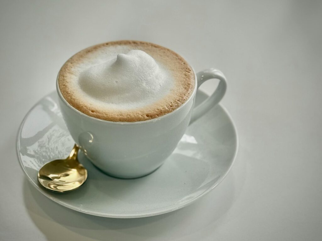 Golden spoon and frothy cappuccino in a white cup create a luxurious coffee setting.